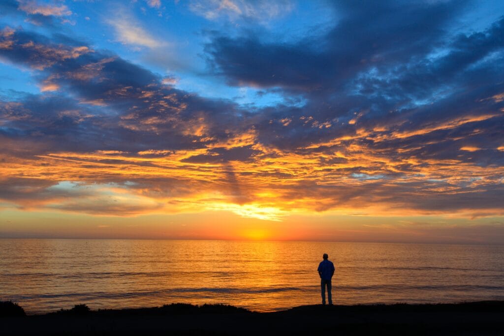 Person silhouette standing on a beach shore with an orange sunset- a cool background